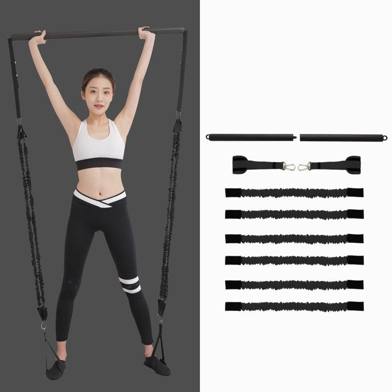 Woman holding a black Pilates bar overhead with resistance cords under her feet, beside the bar, straps and six cords