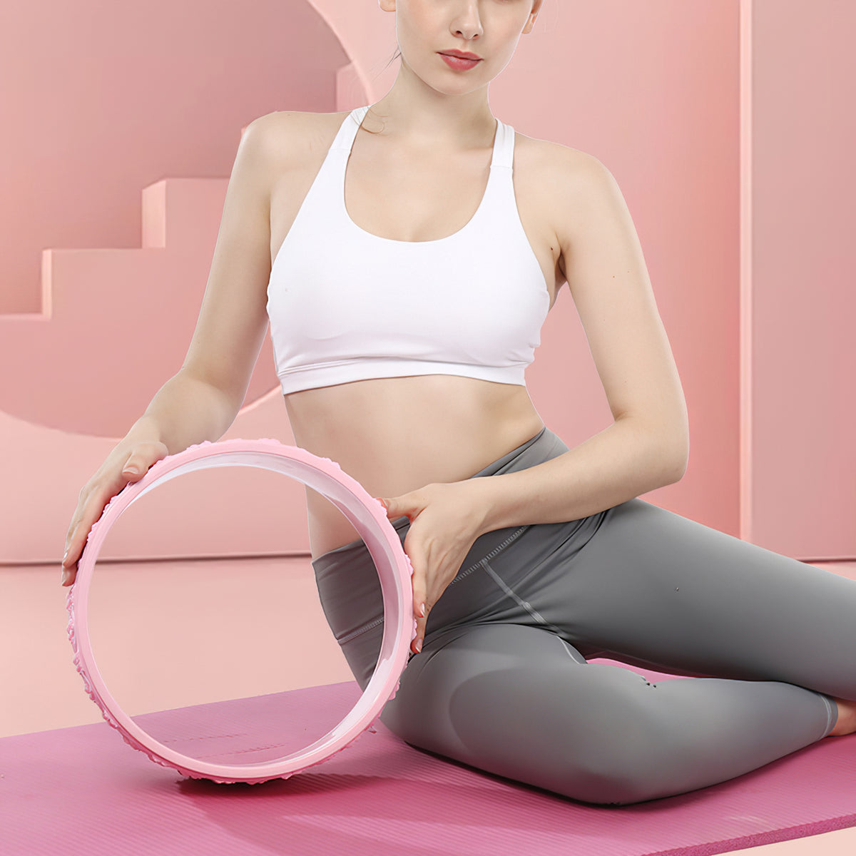 Woman sitting on a pink mat holding a pink textured yoga wheel